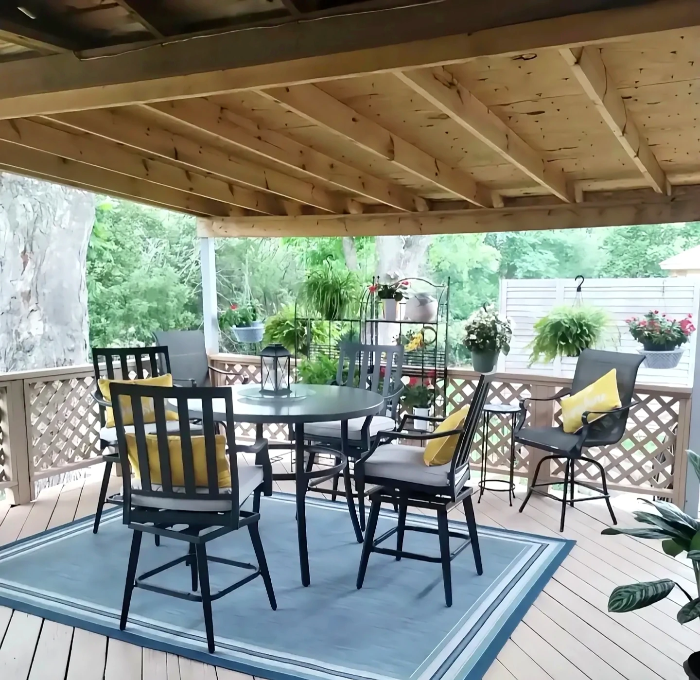 Furnished covered deck after Daltonn’s refinishing work, with finished floor, railing, table, chairs, rug, and plants