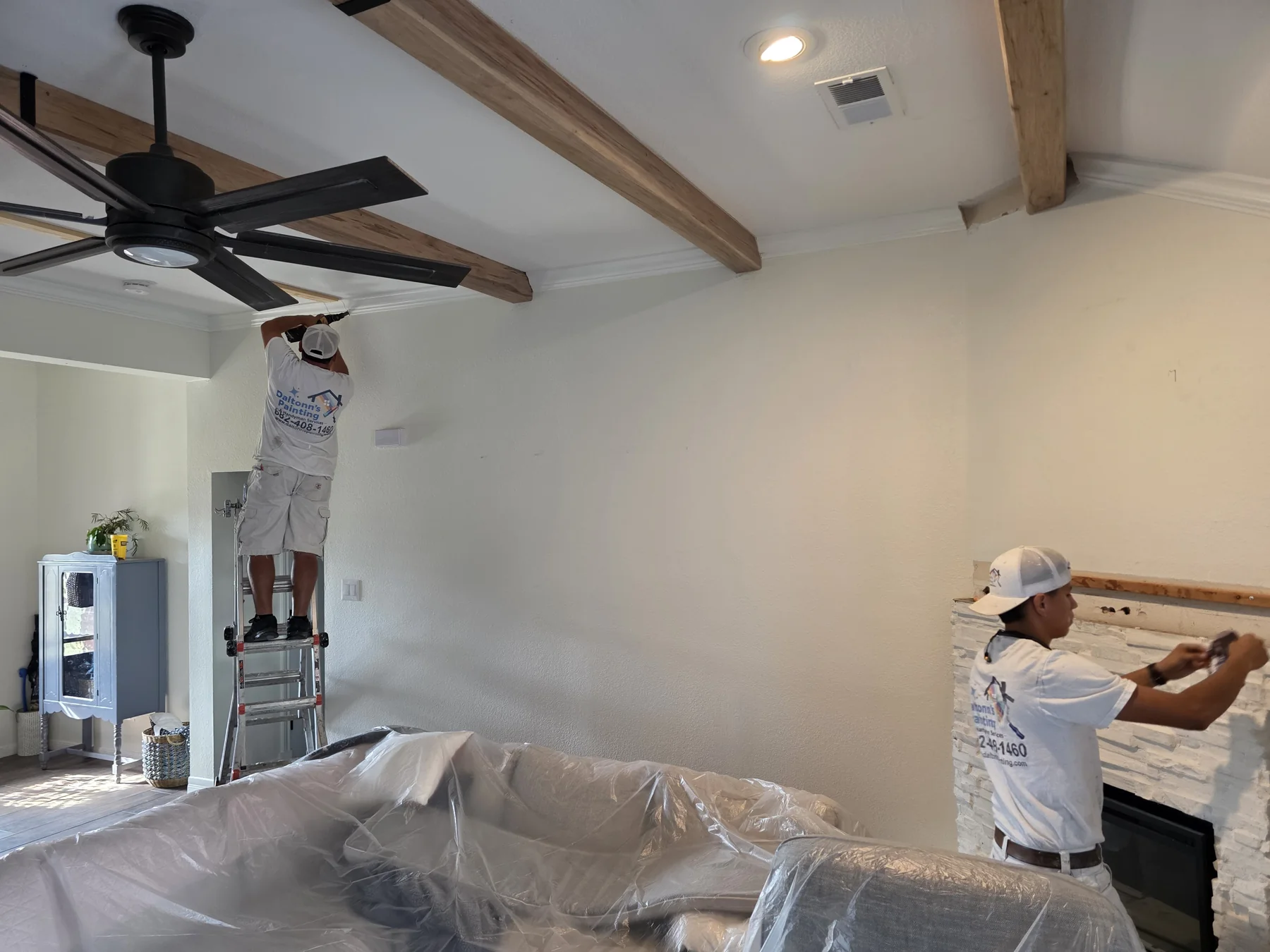 Daltonn and a crew member installing homeowner-provided decorative ceiling beams in a protected living room