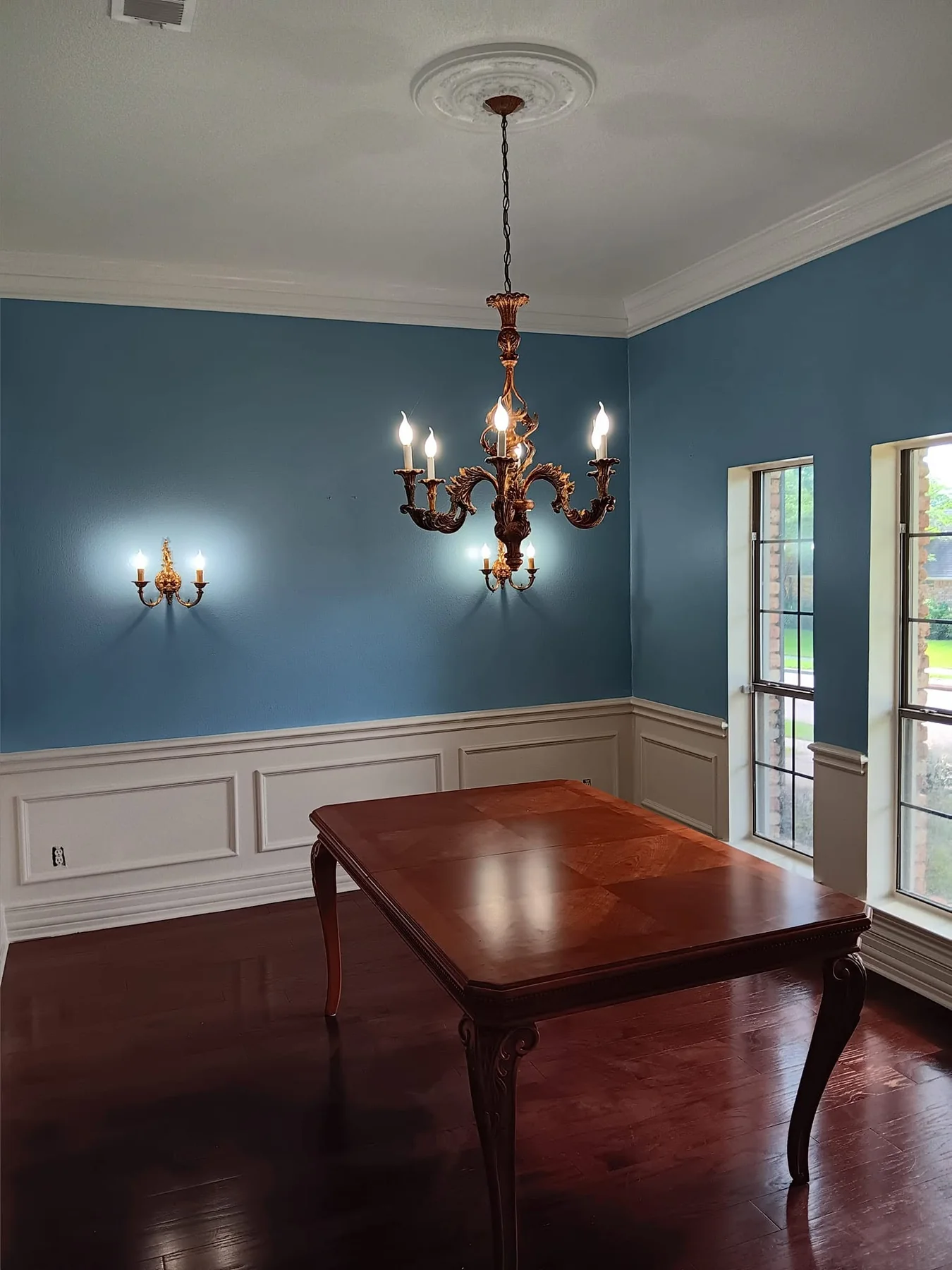 Finished dining room with deep blue walls, white wainscoting, and a chandelier