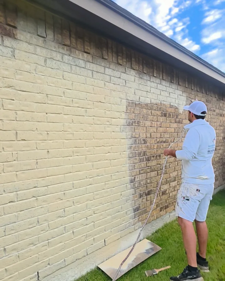 Limewash being sprayed onto the brick, with cream brick next to the last tan section