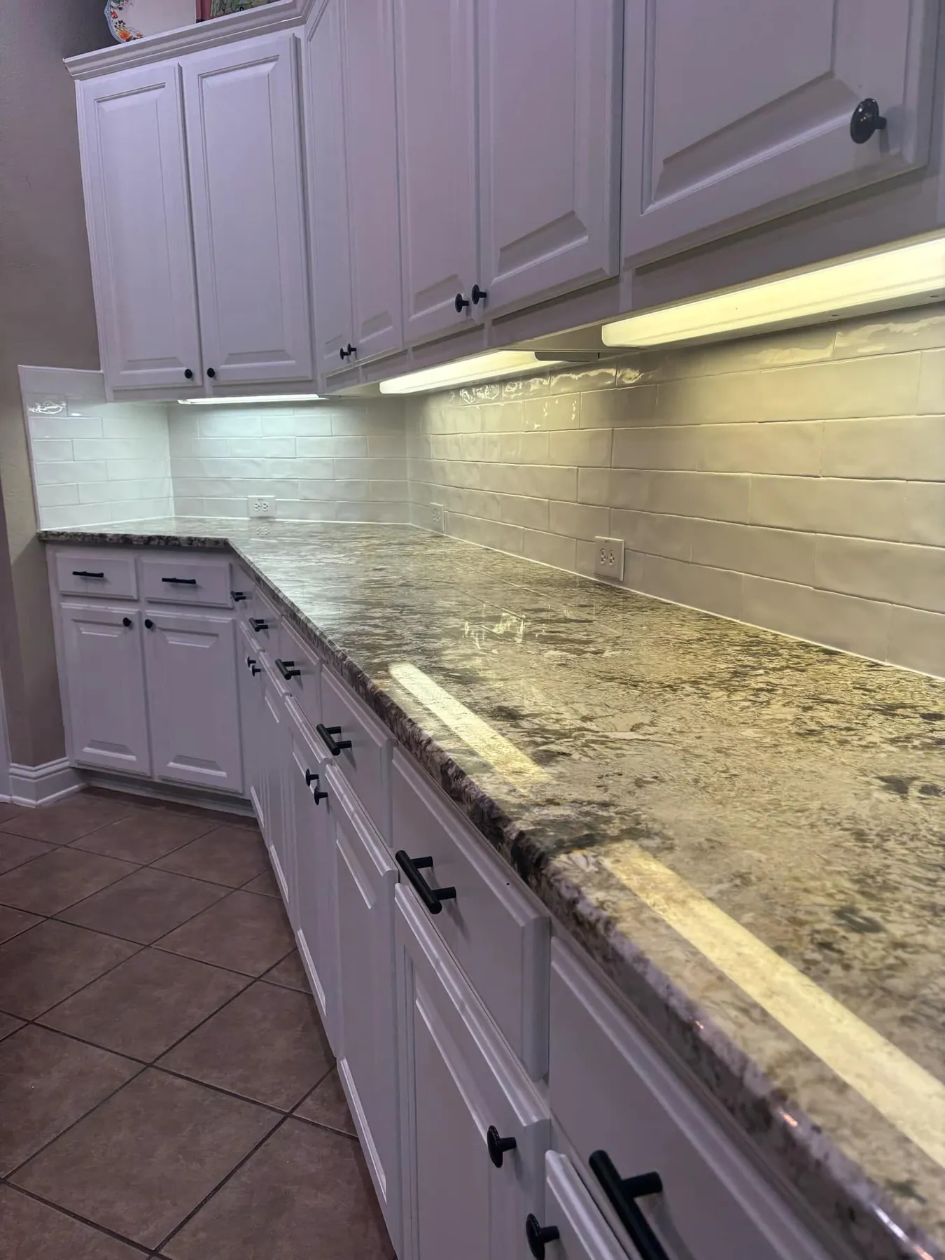 New white tile backsplash running beneath the lit cabinets