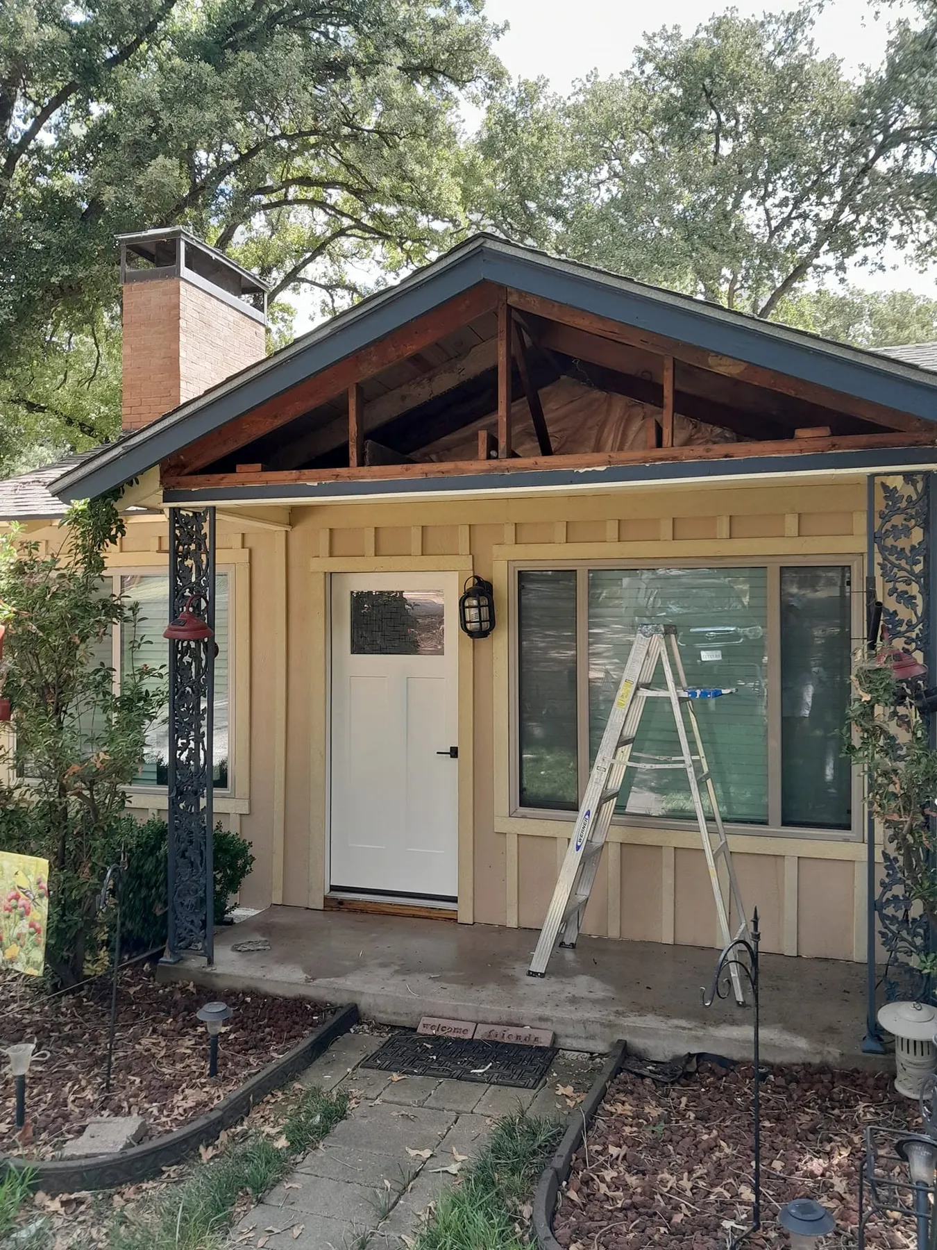 Small cottage front with gable cladding opened and a ladder set up during exterior work