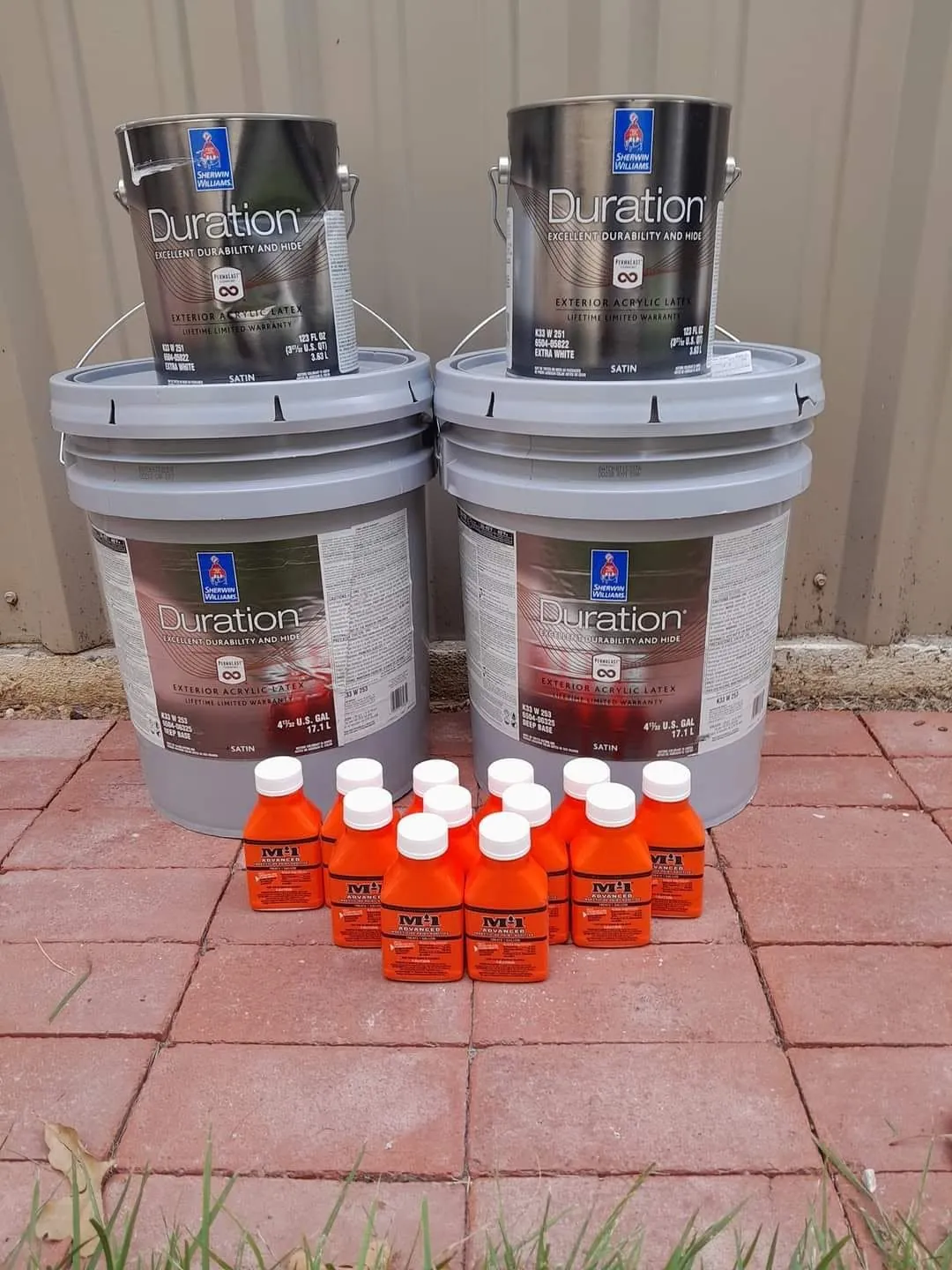 Paint cans and materials staged by the tan board-and-batten siding