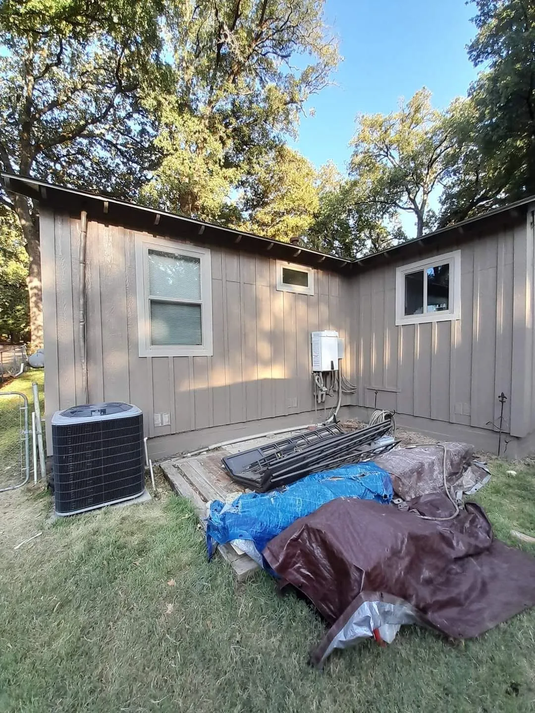 Gray-coated rear cottage wall while tarps and work materials remain