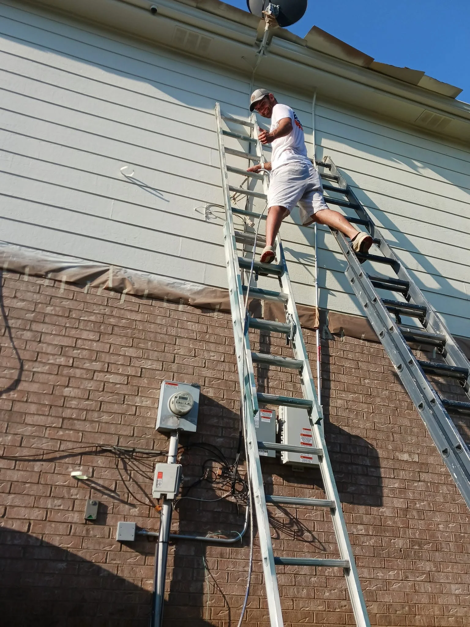 Daltonn's crew member working from a ladder on a two-story brick and siding home